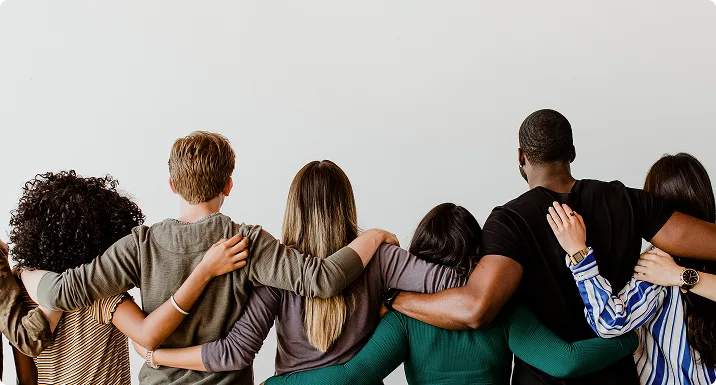 Grupo diverso de pessoas de costas, abracadas pelos ombros, representando uniao e trabalho em equipe
