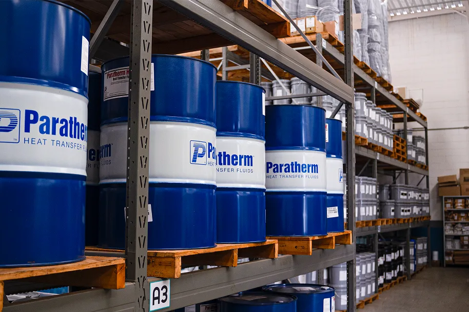 Tambores azuis de fluido termico Paratherm Heat Transfer Fluids organizados em prateleiras de um deposito industrial.